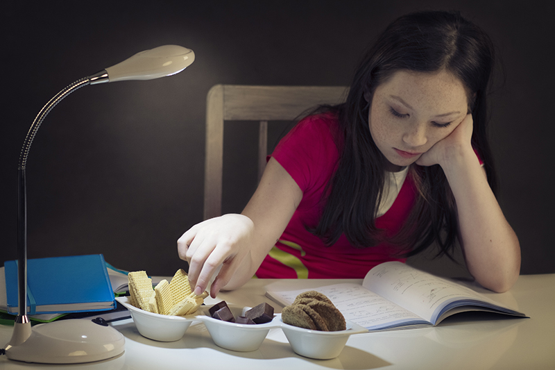 Young girl eating candy while learning in the night (focus is set on hand taking candy)